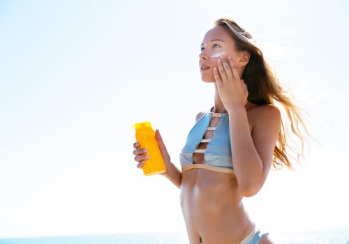 Slim woman applying sunscreen for her face, on the beach