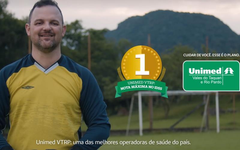Imagem mostra home com uniforme de goleiro, sorrindo, com uma goleira e um campo de futebol ao fundo. Texto diz: Unimed VTRP, nota máxima no IDSS, uma das mellhores operadoras de planos de saúde do Brasil. Cuidar de você, esse é o plano.