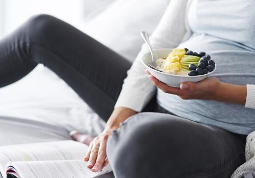 Pregnant woman eating and reading a book at bedroom