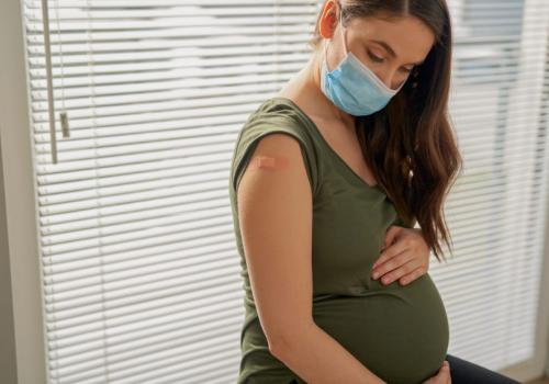 Pregnant caucasian woman sitting with protective mask after vaccination