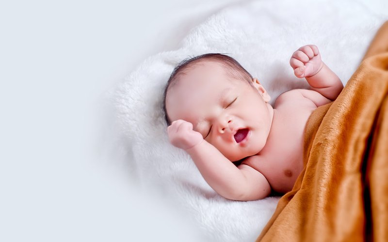 Imagem mostra bebê deitado sobre uma coberta e com uma sobre ele