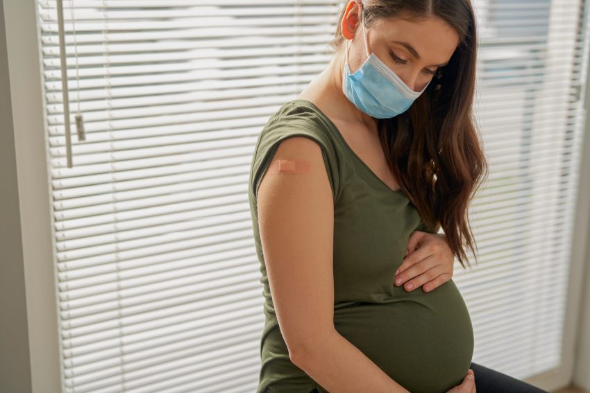 Pregnant caucasian woman sitting with protective mask after vaccination