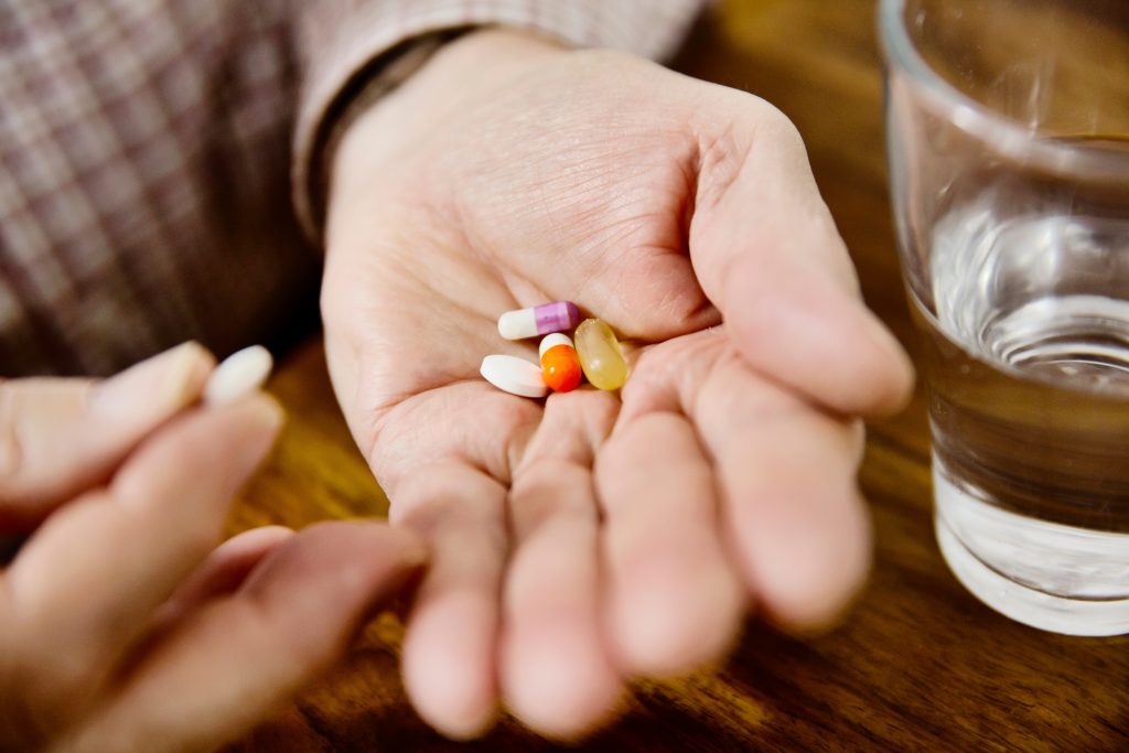 Imagem mostra mão de pessoa segurando múltiplos comprimidos e cápsulas de medicamentos